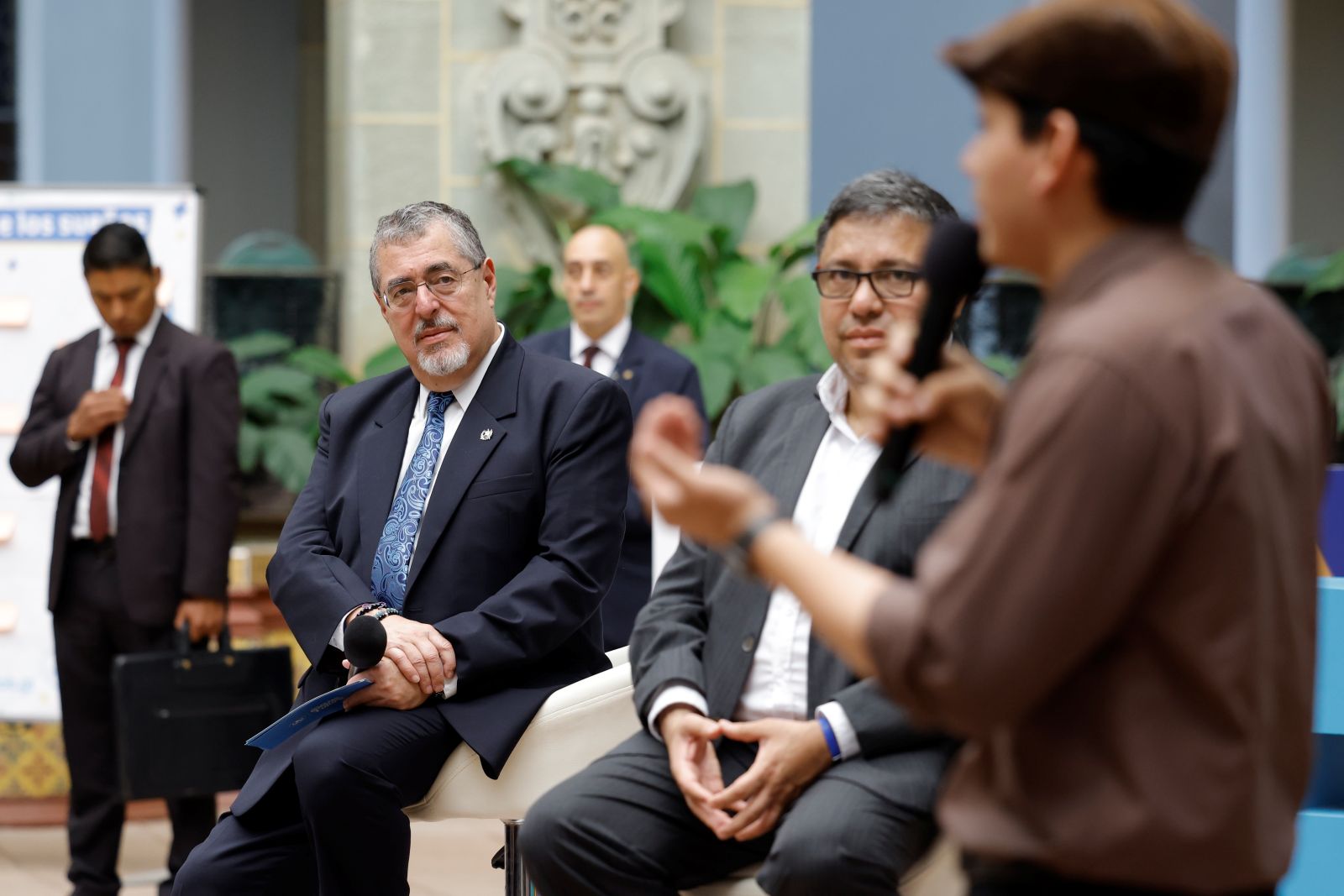 El presidente Bernardo Arévalo y el titular de Segeplan, Carlos Mendoza, escuchan el testimonio de un joven beneficiario del programa Becas por nuestro futuro.
